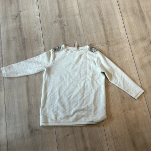 Vit långärmad tröja med detaljer från Pull&Bear - Säljer en vit långärmad tröja från Pull&Bear med snygga mönstrade axeldetaljer. Tröjan har en diskret struktur i tyget och är perfekt för dig som gillar stilrena plagg med en twist.