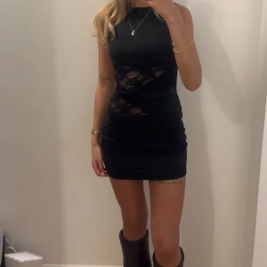 Svart kort klänning med spetsdetaljer - Snygg svart kort klänning med genomskinliga spetsdetaljer i midjan. Ärmlös modell med rund halsringning och figurnära passform. Perfekt för en kväll ute. Endast använd en gång och tvättad🖤