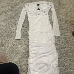 Vit långklänning från Boohoo - Säljer en elegant vit långklänning från Boohoo med långa ärmar och draperade detaljer längs kjolen. Klänningen passar perfekt till studenten eller till somriga eventer. Aldrig använt. 