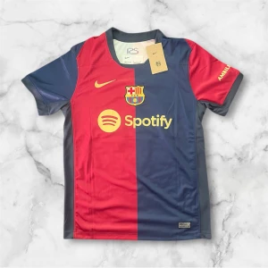 FC Barcelona matchtröja Raphinha 11 - Säljer en officiell FC Barcelona matchtröja från Nike med Raphinha 11 på ryggen. Tröjan är kortärmad och har klassiska blå och röda vertikala fält, klubbmärke och sponsortryck på bröstet samt gula detaljer.