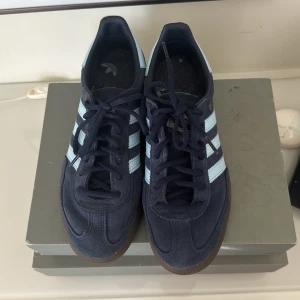 Adidas Spezial sneakers i mörkblå mocka stolek 40 - Säljer ett par Adidas Spezial sneakers i mörkblå mocka med ljusblå ränder och detaljer. Skorna har klassisk Adidas-design med snörning och brun sula. Perfekta för dig som gillar retrostil och streetwear. Otroligt bekväma skor 