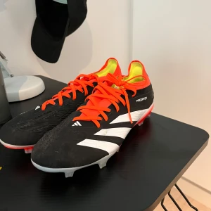 Adidas Predator fotbollsskor med orange snörning - Säljer ett par Adidas Predator fotbollsskor i svart med vita detaljer och orange snörning. 