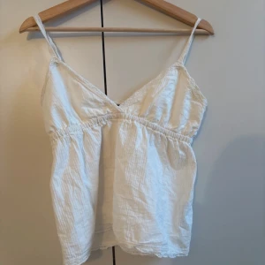 Vit linnetopp med spetsdetaljer - Säljer en söt vit linnetopp med tunna axelband och spetsdetaljer vid bysten. Toppen har en lätt rynkad resår under bysten och är tillverkad i ett tunt, luftigt material. Perfekt för varma dagar! Mycket bra skick!💕💕