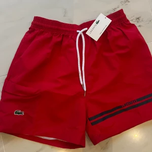 Lacoste badshort - Röda Lacoste badshorts. Oanvända, storlek: M/L