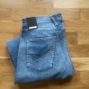 Replay Anbass jeans - Säljer ett par nya klassiska blå jeans från Replay, modell Anbass. Jeansen har fem fickor, normal passform och raka ben. Snygga slitningar och ljus tvätt ger en avslappnad look. Perfekta till vardags med en t-shirt eller hoodie. Som man kan se på jeansen så har de fått en defekt under frakt 