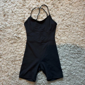 Svart onesie med smala axelband från Aim'n - Säljer en svart onesie från Aim'n med smala korsade axelband och korta ben. Perfekt för träning eller yoga. Materialet är stretchigt och följsamt för maximal rörelsefrihet.