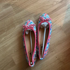 Ballerinaskor stl 37 - Säljer ett par ballerinaskor från Si Barcelona med färgglatt broderat mönster i rosa, blått, gult och orange. Skorna har en söt rosett framtill och rund tå. Knappt använda så i perfekt skick. Stl 37