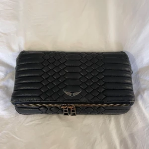 Svart väska från Zadig & Voltaire - Säljer min svart väska från Zadig & Voltaire med kedjerem och snyggt mönstrad yta. Unik design och fint skick! Två kedjor i olika längd medföljer samt dustbag🩷