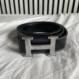 H bälte svart - Säljer ett helt oanvänd svart bälte med spännet H. Bältet är 115cm långt och har 5 hål. Man får även med en metalbit för att göra fler hål. Priset kan diskuteras.