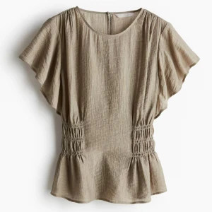 Beige blus med rynkade detaljer intressekoll - Intressekoll på en beige blus från H&M med korta ärmar och rynkade partier i midjan som ger en snygg siluett. Blusen har rund halsringning och lätt volang nedtill. Den är i nyskick med lappen kvar.