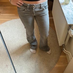 Grå bootcut jeans - Säljer ett par grå bootcut jeans med låg midja och klassiska fem fickor. Jeansen har en snygg tvätt och stängs med dragkedja och knapp. Perfekta för dig som gillar en retro vibe och vill ha ett par jeans som sticker ut lite.