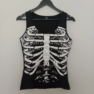 Svart linne med skelettmönster - Coolt svart linne från SHEIN med vitt skelettmönster framtill. Perfekt för dig som vill sticka ut med en alternativ stil. Linnet har breda axelband och är figurnära i modellen.