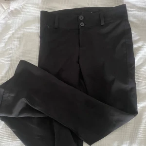 Svarta bootcut kostymbyxor med knappar - Snygga svarta bootcut kostymbyxor med två knappar framtill och fickor med lock och knapp bak. Säljer eftersom att dem inte kommer till användning 💞
