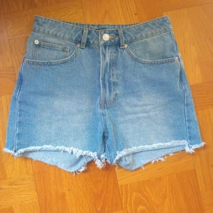 Blå jeansshorts med fransar från BikBok - Säljer ett par klassiska blå jeansshorts från BikBok i storlek S. Shortsen har fransade benslut, fem fickor och normal passform. Perfekta för sommaren och enkla att matcha med olika toppar.