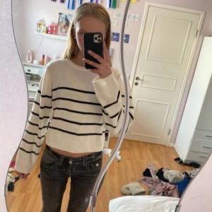 Vit stickad croppad tröja med svarta ränder - Säljer en vit stickad croppad tröja med svarta horisontella ränder. Tröjan har lång ärm, rund halsringning och ribbade muddar. Perfekt för en avslappnad och trendig stil.