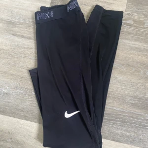 Svarta Nike leggings - Svarta leggings från Nike, Diskret Nike-logga på benet och elastisk midja med Nike-tryck. Perfekta för träning och sportiga aktiviteter. Dom har blivit lite noppriga i midjebandet 