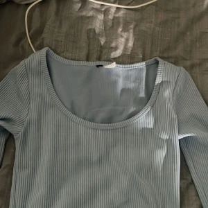 Ljusblå ribbad långärmad topp - Säljer en ljusblå ribbad långärmad topp med rund halsringning. Toppen är i ett mjukt och stretchigt material och har en tight passform. Perfekt att styla med jeans eller kjol för en enkel och snygg look. Passar för s ochså 