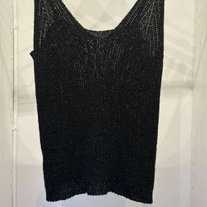 Svart stickad linnetopp - Säljer en svart stickad linnetopp med smala axelband och djup ringning. Toppen är tillverkad i en blandning av viskos och polyester och har en glittrig finish som ger en snygg touch till outfiten.