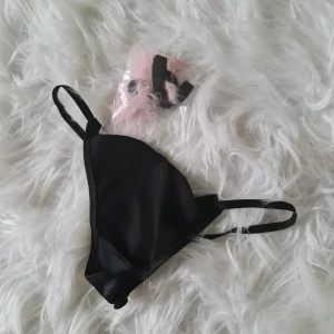 Svarta stringtrosor  från Victoria's Secret - Säljer svarta stringtrosor från Victoria's Secret i glansigt material. Dom är nya med prislapp och har en rosa fluff grej man kan sätta på där bak. Endast tagit ut dom ur plasten för att fota. Oönskad present. Kommer inte öppna den rosa fluffgrejen vill att det ska va så orört som möjligt utifall att någon vill ge bort det i present. 