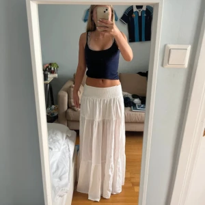 Vit långkjol med resår i midjan - Säljer en vit långkjol med bred resår i midjan. Kjolen har en luftig och flowy passform med flera sömmar som ger ett fint fall. Perfekt för varma dagar och enkel att styla med olika toppar.