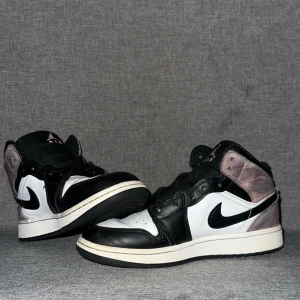 Nike Air Jordans 1 galaxy  - Säljer ett par Nike Air Jordans i svart och vitt med grå/lila detaljer på hälen. Skorna har klassisk hög siluett, svart swoosh och snörning framtill. Perfekta för dig som gillar streetwear och vill sticka ut med en ikonisk sneaker. Äkta 