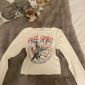 Vit långärmad topp med tryck från STAY - Säljer en vit långärmad topp från STAY med coolt tryck framtill där det står 'Free Spirit' och en örn. Toppen är perfekt för dig som gillar statement-plagg. Knappt använd!