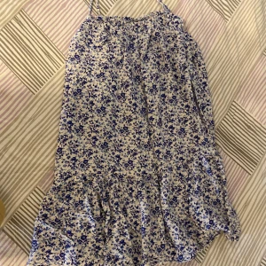 Blommig sommarklänning med volang - Söt blommig klänning i vitt och blått med tunna axelband och volang nertill. Perfekt för varma dagar och har en luftig passform. Klänningen har ett romantiskt blommönster och är lätt att bära.