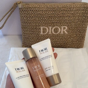 Dior Solar solskyddsset med necessär - Lyxigt solskyddsset från Dior Solar med tre produkter: en skyddande kräm SPF 50, en after sun balm och en skimrande kroppsolja. Kommer i en snygg beige necessär i flätad stil med Dior-logga. Perfekt för stranden eller resan.