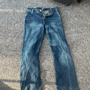 Blå jeansbyxor från Levi's - Klassiska blå jeansbyxor från Levi's med raka ben och normal passform. Byxorna har dragkedja, knappstängning och tydliga kontrastsömmar. Bakfickorna har den ikoniska Levi's-sömmen och röd etikett.