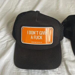 Svart keps från John Hatter & Co med orange skylt - Svart keps med skylten: I DON’T GIVE A FUCK