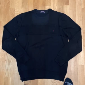 Svart stickad tröja från Tommy Hilfiger - Säljer en svart stickad tröja från Tommy Hilfiger med diskret logga på bröstet. Tröjan har rund halsringning och långa ärmar. Perfekt för en stilren och enkel look. Pris kan diskuteras. Trotts att det står XL passar den som L
