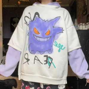 Vit och lila hoodie med Gengar-tryck - Säljer en oversized hoodie i vitt och lila med ett stort tryck av Gengar på framsidan. Hoodien har långa ärmar i lila och en mysig huva. Perfekt för dig som gillar Pokémon och vill ha en unik och färgglad tröja.