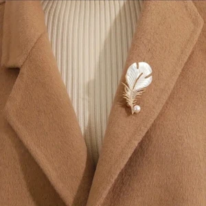 Elegant brosch med pärldetalj - Snygg brosch i form av ett blad med en glittrig fjäder och en pärla. Perfekt för att ge en touch av elegans till din outfit. Broschen har en vit och guld färgkombination som gör den lätt att matcha.