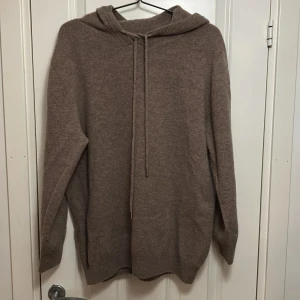 Brun stickad hoodie - Mysig beige stickad hoodie med långa ärmar och justerbar snörning i huvan. Perfekt för kyliga dagar och ger en avslappnad stil. Passar bra till jeans eller leggings. lite krympning i ärmarna 