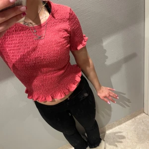 Rosa ribbad topp - Säljer en snygg röd ribbad topp med korta ärmar och volangdetaljer vid ärmslut och nederkant. Perfekt för en trendig look!