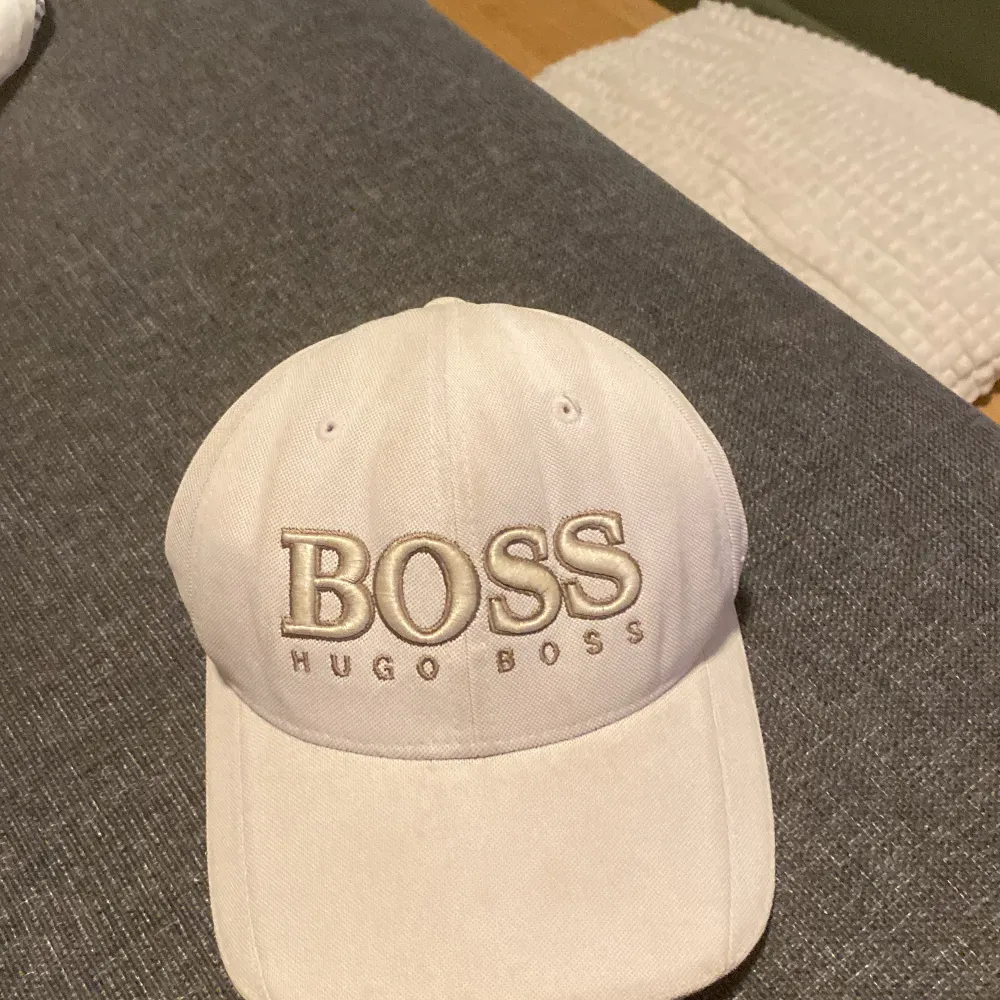 Snygg vit keps från Hugo Boss med broderad logotyp framtill. Kepsen har en justerbar rem baktill för perfekt passform. Perfekt för en stilren look.. Asusteet.