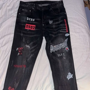 Svarta jeans med tryck från Dsquared2 - Unika svarta jeans från Dsquared2 med coola tryck och broderier i vitt och rött. Jeansen har en straight passform och är tillverkade i Italien. Perfekta för dig som vill sticka ut med en edgy stil. Kan fixa mer bilder och knappen gick av men jag har den fortfarande om någon vill fixa. PRISET KAN DISKUTERAS 