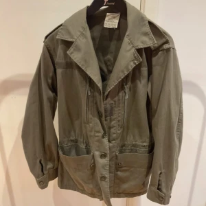 Grön jacka med knappar - Säljer en grön jacka med knappar och stora fickor framtill. Jackan har en klassisk krage och långa ärmar. Perfekt för en avslappnad stil.