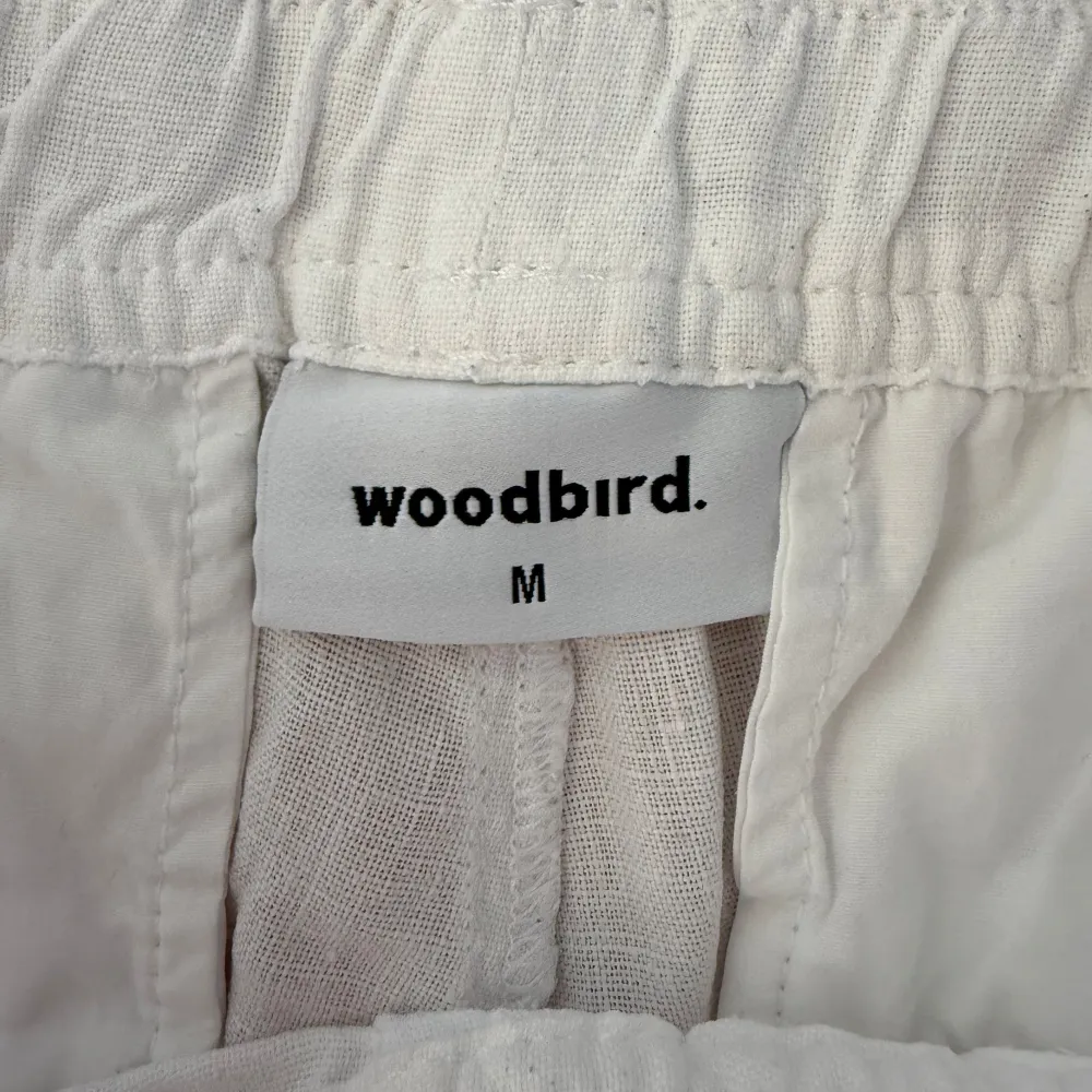 Säljer ett par vita linnebyxor från Woodbird i storlek M. Byxorna har en avslappnad passform med elastisk midja och dragsko för justering. Perfekta för varma dagar med sitt lätta och luftiga material. Nypris 1000kr och mitt 200kr!!!!. Farkut & Housut.