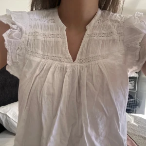 vit blus med volangdetaljer 🤍 - säljer en söt vit blus med volangdetaljer och korta ärmar. blusen har en v-ringad design med spetsdetaljer på bröstet. perfekt för en somrig look!