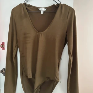 Brun långärmad bodysuit - Snygg brun långärmad bodysuit med djup v-ringning. Perfekt för lager-på-lager eller att bära som den är. Materialet är mjukt och stretchigt för en bekväm passform.