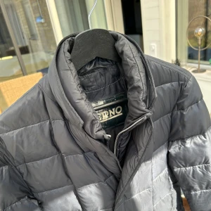Blå pufferjacka från Herno - Säljer en stilren blå pufferjacka från Herno. Jackan har en quiltad design med knappar framtill och en hög krage för extra värme. Perfekt för kyligare dagar.
