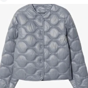 Grå quiltad jacka - Snygg grå quiltad jacka med rund hals och knappar framtill. Jackan har en unik bubbeldesign och långa ärmar. Skriv för bilder eller mer info.