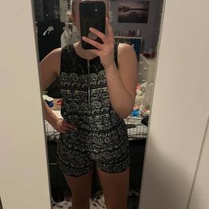 Mönstrad jumpsuit - Snygg jumpsuit med ett detaljerat mönster i blått och beige. Den har en dragkedja framtill, spetsdetaljer vid axlarna och fickor på sidorna. Perfekt för en avslappnad stil i sommar💖