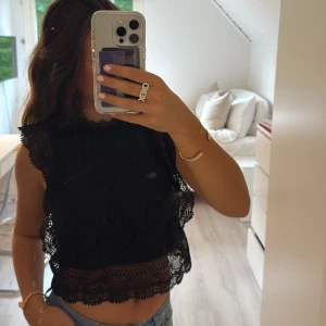 Svart spetsblus  - Elegant svart spetsblus från ONLY. Blusen är ärmlös med spetsdetaljer och croppad passform. Perfekt till fest eller tjejkväll. 