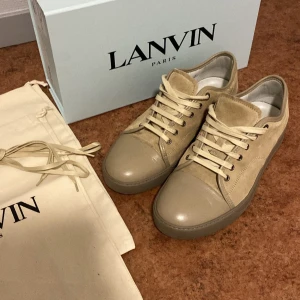 Lanvin skor - Snygga beige sneakers från Lanvin med snörning och en stilren design. Skorna har en kombination av skinn och mocka vilket ger dem en exklusiv känsla. Perfekta för en trendig look. Storlek 44, Size UK 9. Box, påse och extra snören medföljer.