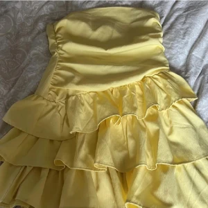 Gul axelbandslös klänning - Säljer en söt gul axelbandslös klänning med volanger. 