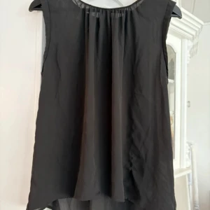 Svart ärmlös blus från Gina Tricot - Säljer en elegant svart ärmlös blus från Gina Tricot. Blusen har en lös passform och ett stilrent fall. Perfekt för både vardag och festliga tillfällen. 🖤