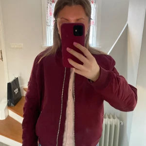 Vinröd bomberjacka - Säljer en snygg vinröd bomberjacka med dragkedja framtill och på ärmen. Jackan har en klassisk bomberstil med ribbade muddar vid ärmslut och nederkant. Perfekt för en cool och avslappnad look.
