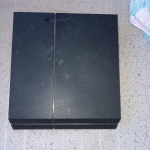 Svart Ps4 spelkonsol - Säljer en svart ps4 spelkonsol med en stilren design. Konsolen har flera portar på baksidan för anslutningar och en diskret logotyp på ovansidan. Perfekt för gaming och underhållning.